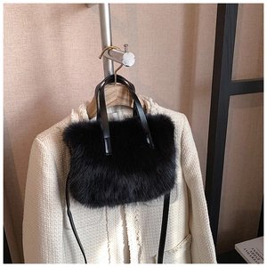 Detail of black faux fur handbag with leather straps against a tweed jacket background