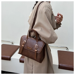 Detail of vintage brown leather bag with gold buckles worn with a beige trench coat
