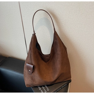 Detail of a dark brown suede hobo bag with a heart charm on a black leather sofa