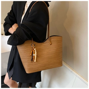 Détail d'un sac cabas tissé marron avec une décoration de breloque en perles de bois