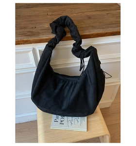 Detailed close-up of a black suede crescent bag with pleated straps on a wooden stool
