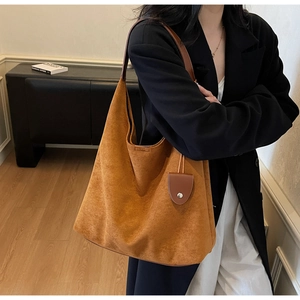 Brown suede tote bag shown on shoulder in a minimalist modern interior setting