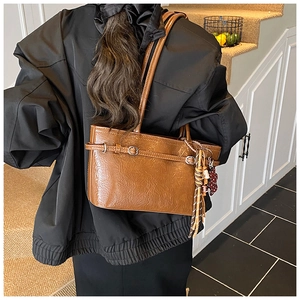 Close-up of brown vintage leather tote bag with metallic buckle and woven tassel detail