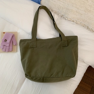Top view of large olive green canvas tote bag on white bedding with purple gloves