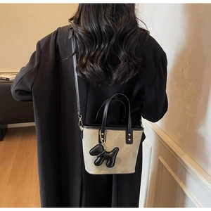 Crossbody bucket bag in apricot grey leather featuring a cute black puppy charm accessory