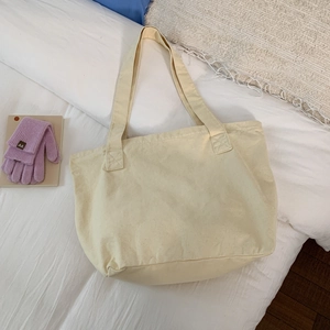 Close-up of beige canvas tote bag on white bedding with purple knit gloves accessory