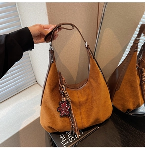 Gros plan sac hobo en daim marron avec breloque ours léopard et pompon sur un magazine