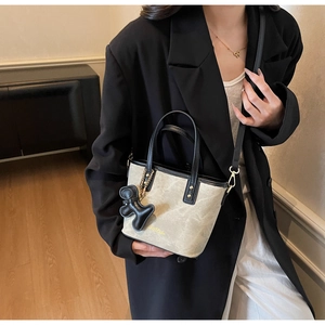 Detail of beige tote bag with black leather trim, puppy charm and golden M'Dolin logo