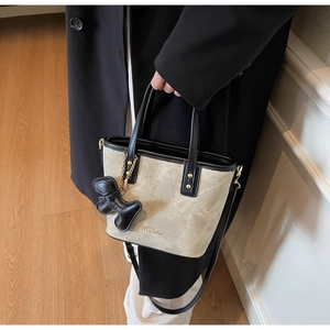 Detailed shot of beige and black bucket bag with gold lettering and charm