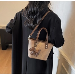 Detail of a brown vintage patterned mini tote bag featuring a leather dog charm