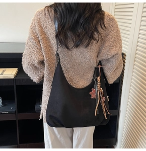 Détail du sac hobo en daim noir avec breloque ours léopard et pompon porté par un mannequin