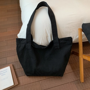 Minimalist large black canvas tote bag shown on a wooden floor in a cozy home setting