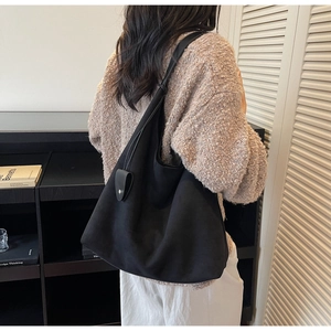 Detail view of a black oversized Hobo tote bag showing draped shape and shield buckle charm