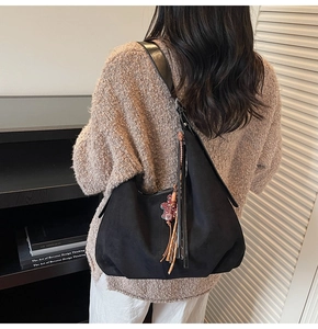 Détail du sac hobo en suédine noire avec breloque cochon rouge et accessoire à franges