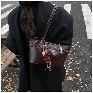Detail of dark brown patent leather shoulder bag with chic leopard bear charm accessory