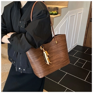 Détail d'un sac cabas marron à texture tissée avec bandoulière et pendentif en perles
