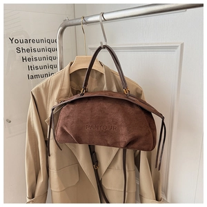 Detail of suede boston bag with embossed logo and golden hardware on coat rack