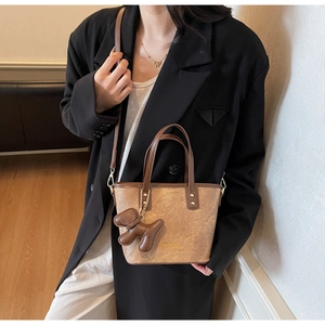 Detail of brown bucket bag with dark leather handle and cute puppy charm on model