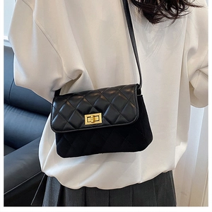Detail of black quilted crossbody bag with gold twist lock on casual white outfit
