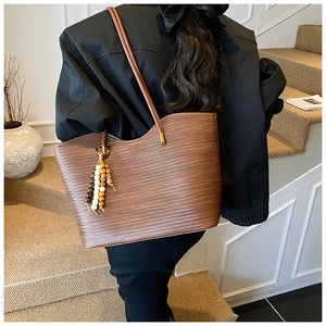 Sac fourre-tout tissé marron avec pompon en perles porté par un mannequin en intérieur