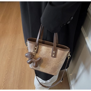 Close-up of brown suede bucket bag with gold logo, leather trims and puppy charm detail