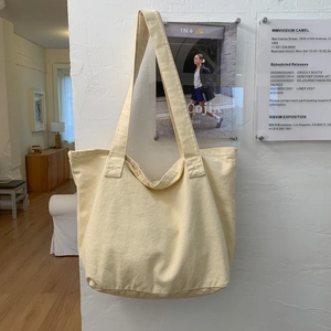 Detail of wide shoulder strap and spacious cream canvas tote bag on wall