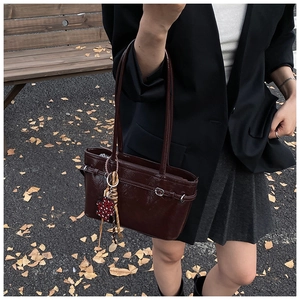Detail of dark brown patent leather tote bag with leopard heart charm and buckle accent