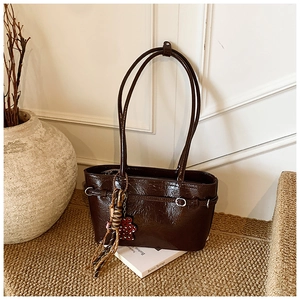 Detail of dark brown leather tote bag with tassel and bear charm on woven rug