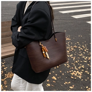 Détail du sac cabas marron foncé avec texture tressée et breloque en perles de bois sur l'épaule