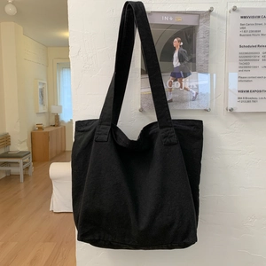 Close-up of minimalist black canvas tote bag hanging on a white textured wall