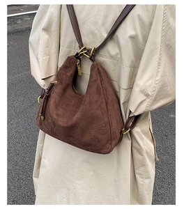 Detail of vintage brown suede hobo bag with gold hardware worn over a beige coat
