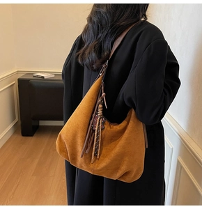 Détail du sac hobo en daim fauve avec ornement de gland et breloque tissée sur la lanière