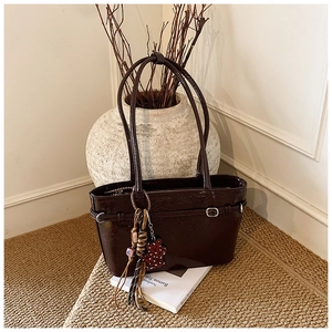 Macro detail of wine red patent leather handbag with decorative clover charm and tassels