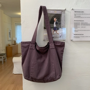 Detailed texture of deep purple canvas tote bag hanging on a white textured wall