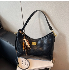 Dettaglio borsa in pelle nera trapuntata con chiusura dorata e ciondolo in legno