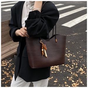 Détail d'un grand sac cabas tissé marron foncé avec pompon en perles de bois colorées