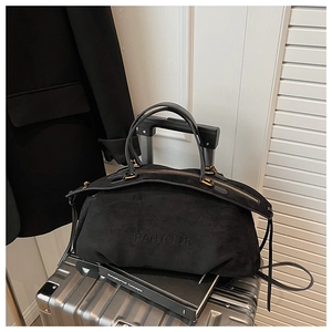 Detail of black suede Boston bag with gold hardware on a metallic suitcase