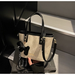 Detailed view of beige crossbody tote bag with black trim and puppy charm on dark books