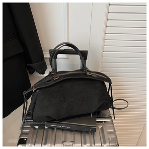 Close-up of black suede Boston bag with embossed logo on a metallic suitcase