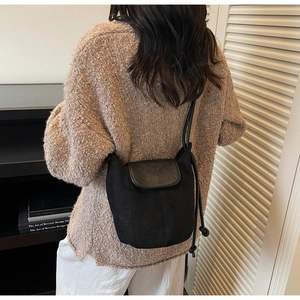 Détail d'un sac à bandoulière minimaliste noir mat porté avec un gros pull en maille