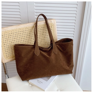 Detail of dark brown suede tote bag with slim handles on a chair in a cozy setting