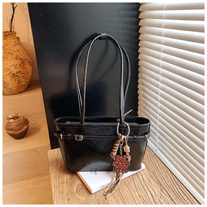 Detail of glossy black vintage tote bag with decorative charms in a sunlit interior