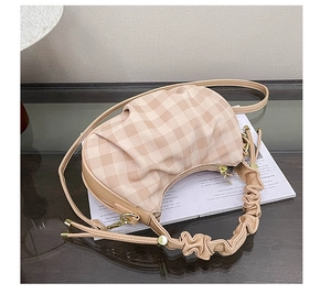Detail of beige plaid pleated crescent bag with leather piping and adjustable strap
