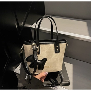 Close-up of beige canvas bucket bag with black leather trim and poodle charm on design books
