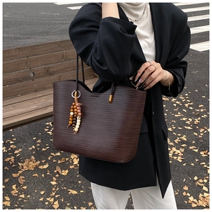 Détail du sac cabas tissé marron foncé avec un pendentif décoratif en perles de bois