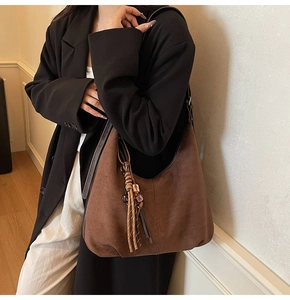 Détail d'un sac hobo en daim marron foncé avec pompon tressé et texture mate douce