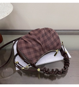 Detail of checkered hobo bag in dark coffee with ruffled handle on a glass table