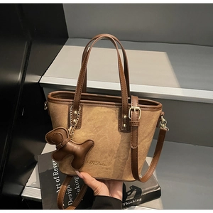 Close-up of brown suede tote bag with leather straps and a decorative dog charm