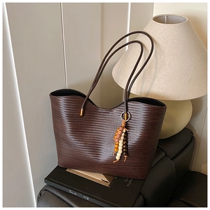 Détail du sac cabas tressé marron foncé avec pompon perlé et fines anses rondes