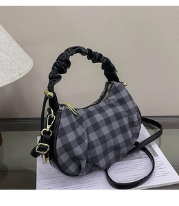 Detail of checkered hobo bag featuring a black ruched handle and gold-tone hardware accents